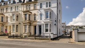 A row of white townhouses with bay windows, a blue door, and a small front garden. - 2 Bed - Hoe Heights by Smart Welcomes (Plymouth)