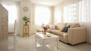 A modern living room with a beige sofa, a white coffee table, a potted plant, and a clock on the wall. - Bocagrande - 2BR with panoramic ocean view (Cartagena de Indias)