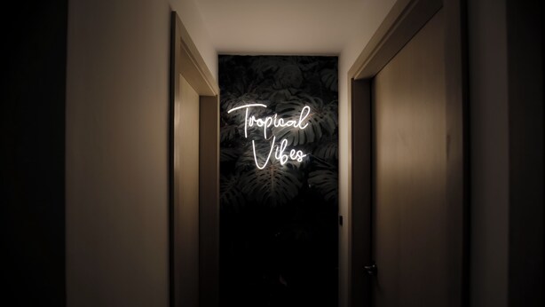 A hallway with a neon sign that reads "Tropical Vibes" against a dark background with leaf patterns. - Bocagrande - 2BR with panoramic ocean view (Cartagena de Indias)