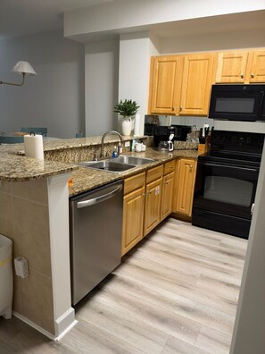 Una cocina moderna con encimeras de granito, electrodomésticos de acero inoxidable, armarios de madera y lavavajillas integrado.