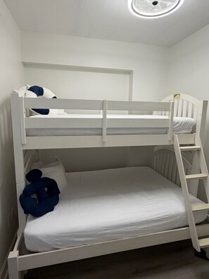 Una cama litera con escalera, ropa de cama blanca y una lámpara en el techo.