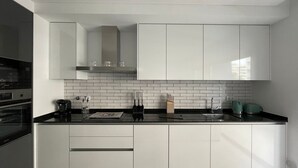 Une cuisine moderne avec des meubles blancs, un plan de travail noir et un pare-feu en carrelage.