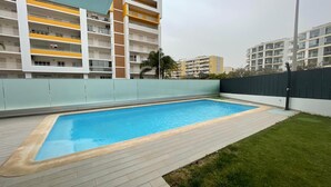 Une piscine rectangulaire avec une terrasse carrelée, entourée d’un petit muret et d’une zone herbeuse.