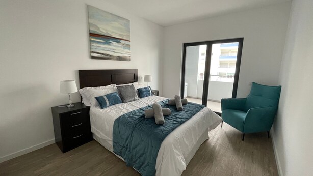 Une chambre moderne avec un lit, des tables de chevet, une chaise et une grande fenêtre.