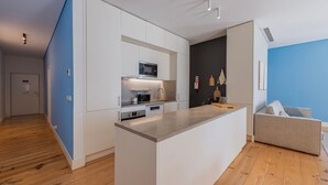 A modern kitchen with white cabinets, a microwave, and a built-in oven. There's a wooden floor and a blue accent wall.