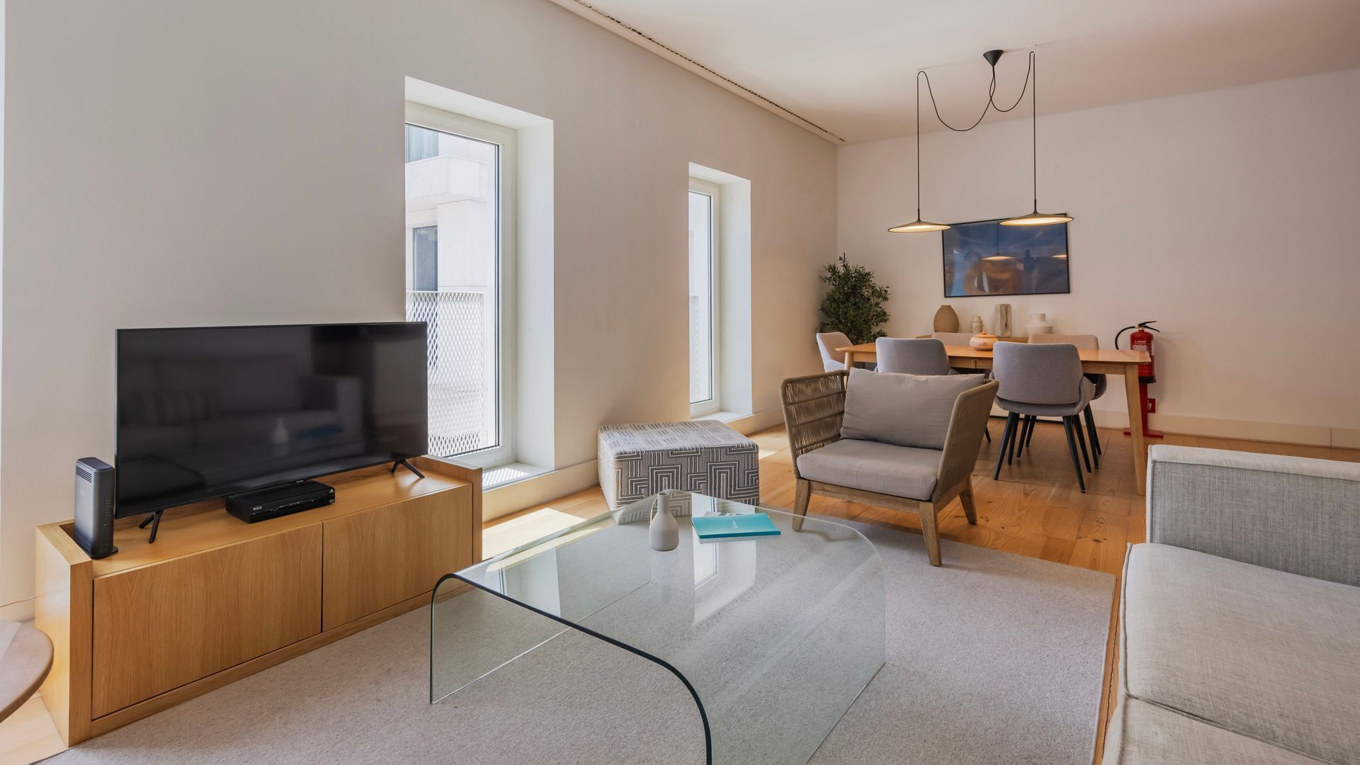 Un salon moderne avec un téléviseur à écran plat posé sur une console en bois, une table basse en verre et un coin repas comprenant une table et des chaises.