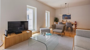 Ein modernes Wohnzimmer mit Flachbildfernseher auf einer Holzkonsole, einem Glastisch und einem Essbereich mit Tisch und Stühlen.