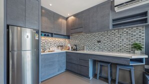 Una cocina moderna con armarios grises, un refrigerador de acero inoxidable, salpicadero de azulejos y una barra con taburetes.