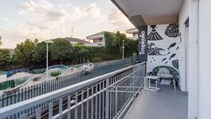 Un balcon avec une balustrade blanche, une chaise et un mur orné de motifs de feuilles tropicales.