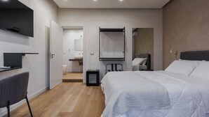 Une chambre d’hôtel moderne dotée d’un grand lit, d’un bureau avec une chaise, d’un téléviseur fixé au mur et d’une salle de bain visible à travers une porte ouverte.