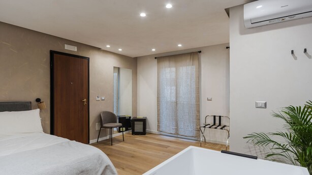 Una habitación de hotel moderna con dos camas, un ventanal con cortinas, unidad de aire acondicionado integrada y una pequeña zona de estar.