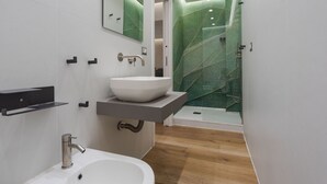 Un baño moderno con un lavamanos blanco, un espejo y una zona de ducha con pared texturizada de color verde.