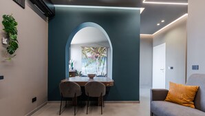 A modern living room with a dining area, featuring a large arched window, a sofa, and a dining table with chairs.