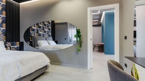 A modern bedroom with a curved mirror, a bed, a desk, and a chair.