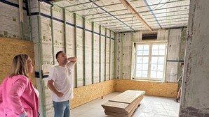 Habitación en construcción con techo y paredes a la vista, suelo de madera y una ventana.