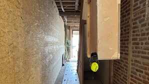 Una obra en construcción con vigas de madera expuestas, suelo de hormigón y materiales de construcción.