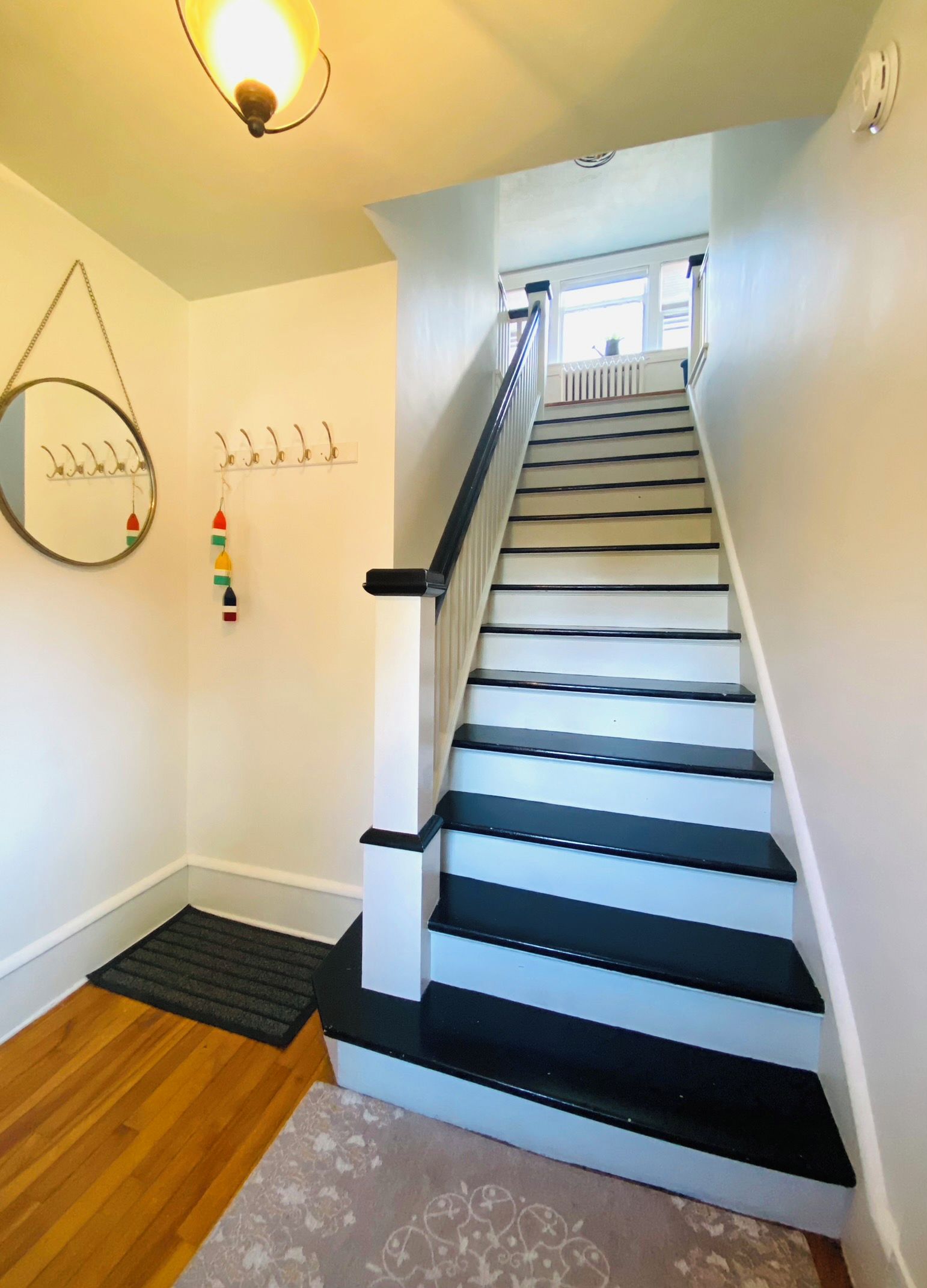 A staircase with black steps and white walls, a mirror, and a wall-mounted light fixture.