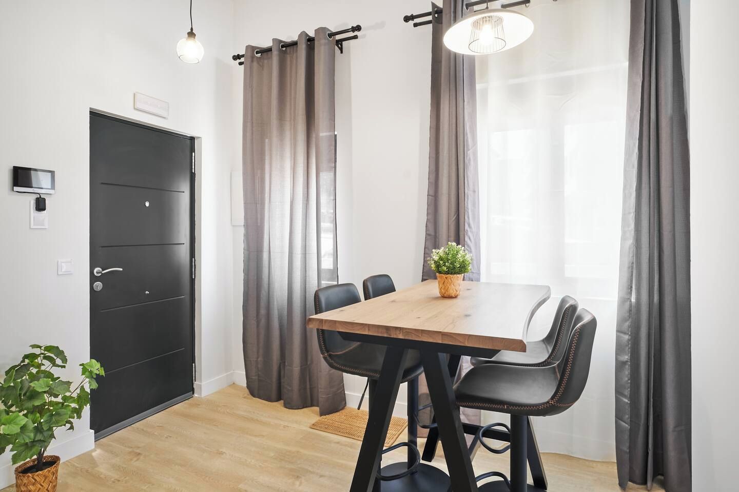 A modern room with a wooden table, black chairs, a potted plant, and a black door.