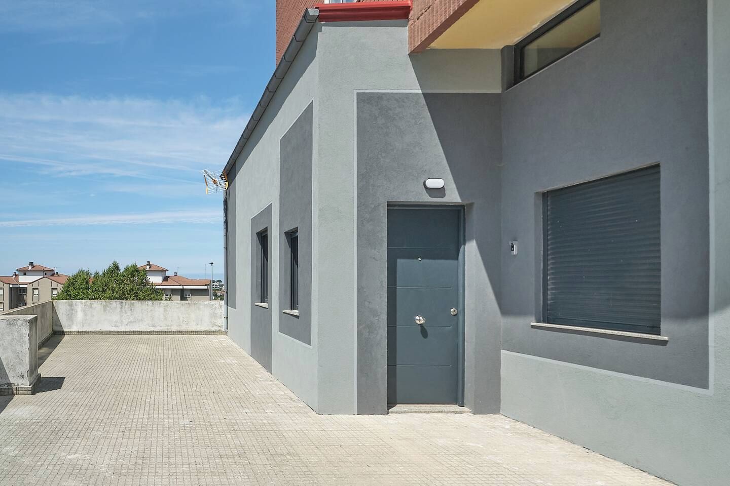 A modern building with a grey facade, a blue door, and a window with a shutter.