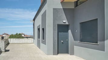 A modern building with a grey facade, a blue door, and a window with a shutter.
