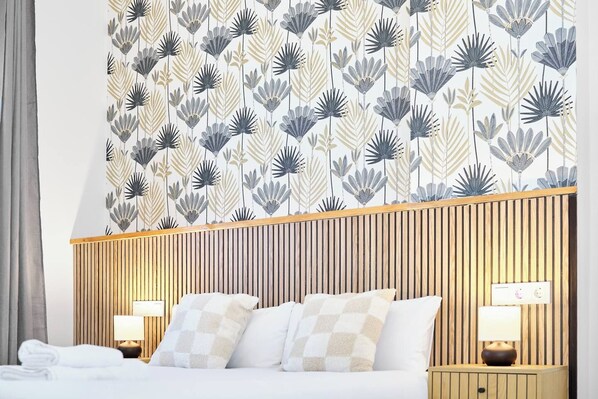 A hotel room with a bed, two bedside lamps, a wooden headboard, and a patterned wallpaper.