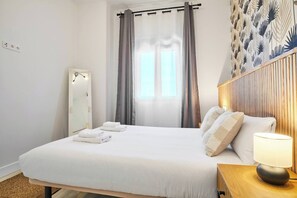Habitación de hotel con una cama grande, una mesita de noche con lámpara, un espejo y una ventana con cortinas.
