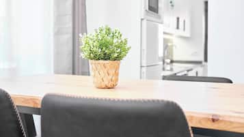 A dining table with a woven plant pot in the center, black chairs, and a kitchen in the background.