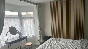 A bedroom with a bed, a desk with a chair, a window with curtains, and a radiator. - Green Lane 1-bed Apartment - Sleeps 4 & Pets Ok (Leicester)