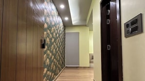 A hallway with wooden flooring, a floral wallpapered wall, and a closed door. - Sunrise studio 2 (Delhi)