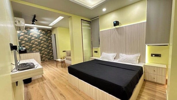 A modern bedroom with a large bed, bedside tables, a wardrobe, and a small seating area. - Sunrise studio 2 (Delhi)