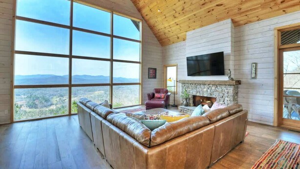 A spacious living room with a large window, a stone fireplace, and a leather sofa.