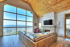 A spacious living room with a large window, a stone fireplace, and a leather sofa.
