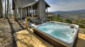 A wooden cabin with a hot tub and deck overlooking a mountainous landscape.