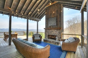 A covered outdoor seating area with wicker furniture, a stone fireplace, and a view of the mountains.