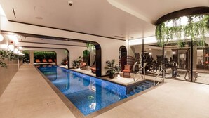 Un área de piscina interior moderna con una piscina larga y estrecha, sillones de descanso y equipo de ejercicio.