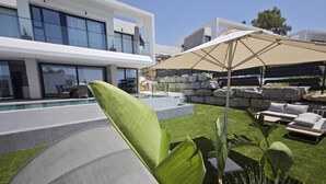 Ein moderner Außenbereich mit Pool, Liegestühlen und einem großen Sonnenschirm.