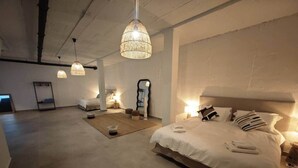 Ein geräumiges Schlafzimmer mit einem großen Bett, einer kleinen Sitzecke und Pendelleuchten.