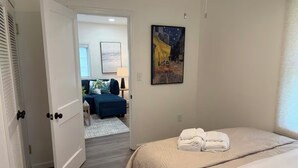 A hotel room with a bed, a painting, and a view into another room with a blue sofa and a lamp. - Cozy and Convenient- 5 min to Airport (North Charleston)