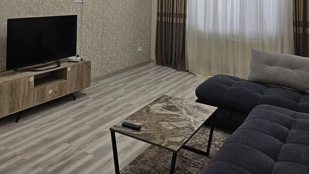 Moderni olohuone, jossa on litteänäyttöinen televisio, sohva, sohvapöytä ja kattokruunu.