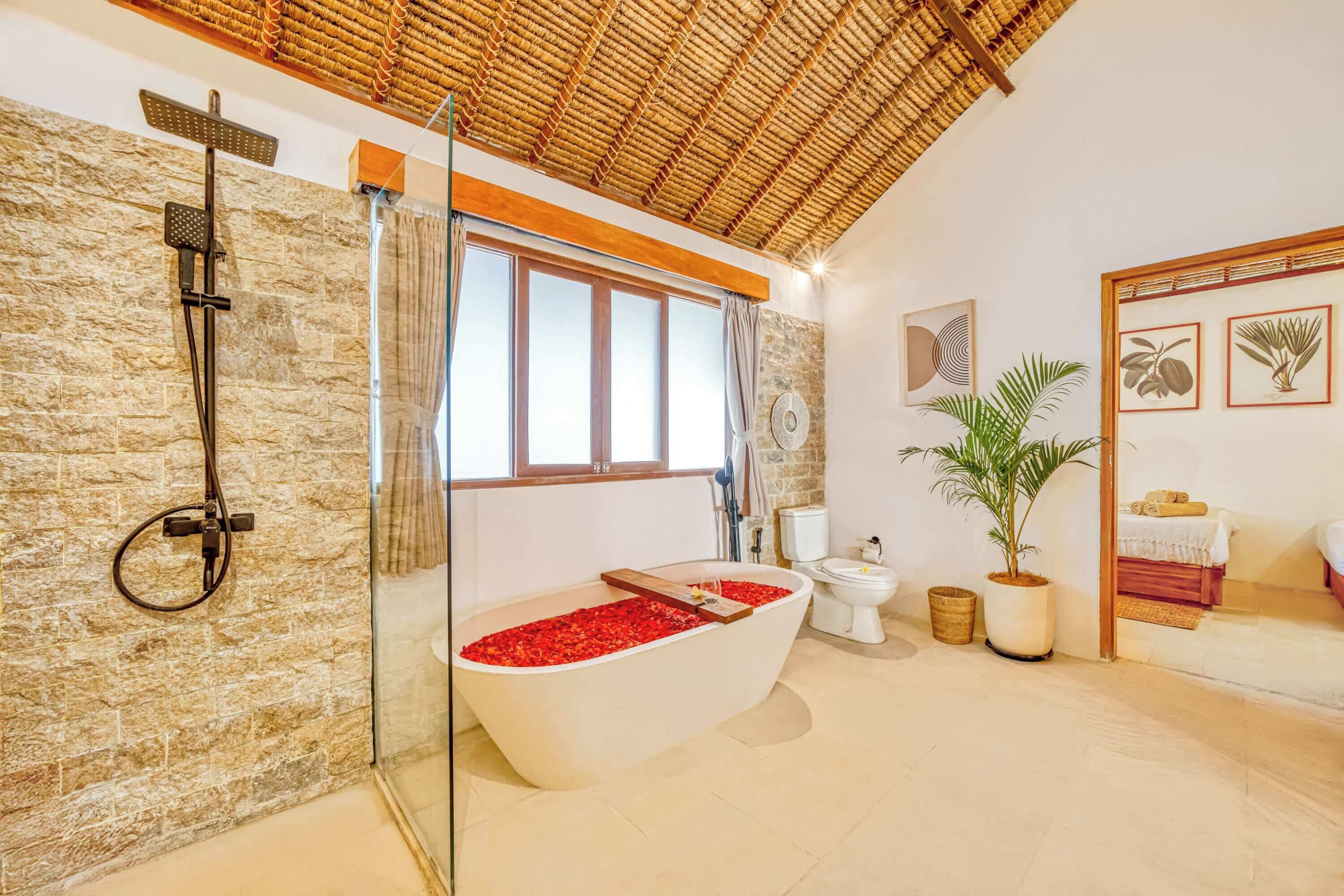 A bathroom with a freestanding bathtub, a glass-enclosed shower, a toilet, and a potted plant.