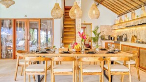 A spacious dining area with a large wooden table and chairs, surrounded by hanging wicker light fixtures.