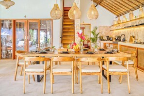 A spacious dining area with a large wooden table and chairs, surrounded by hanging wicker light fixtures.
