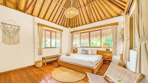 A spacious bedroom with a large bed, wooden flooring, a woven ceiling, and large windows.