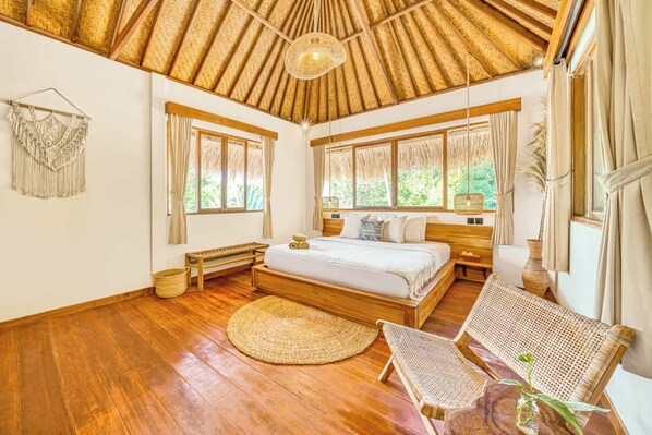 A spacious bedroom with a large bed, wooden flooring, a woven ceiling, and large windows.