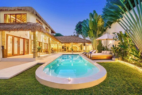 Una villa moderna con piscina, mobiliario exterior y exuberante vegetación tropical.