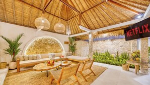 A modern living room with a thatched ceiling, a large stone wall, and a Netflix sign. - Villa Barcelona - 6BDR, lush garden, private pool (Kabupaten Badung)
