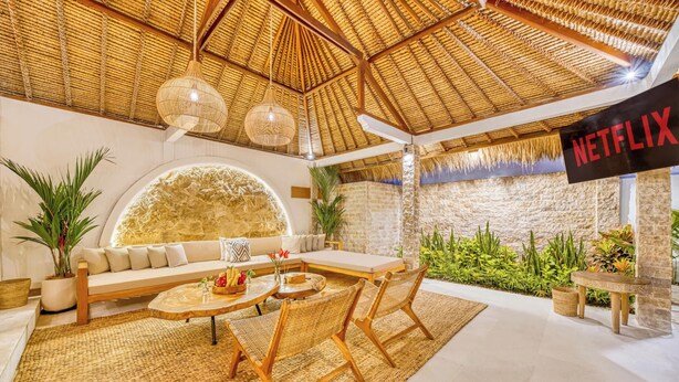 A modern living room with a thatched ceiling, a large stone wall, and a Netflix sign.