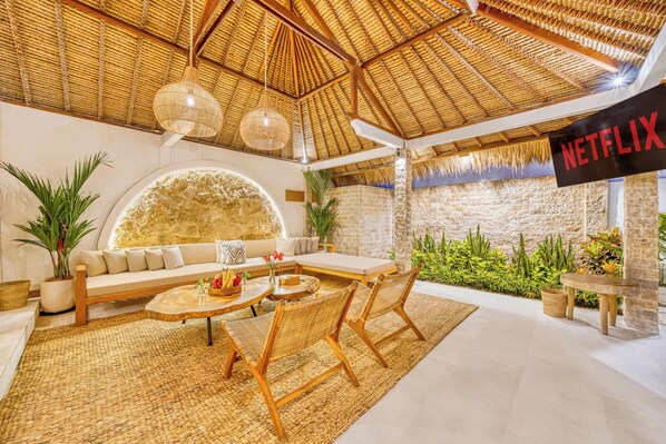A modern living room with a thatched ceiling, a large stone wall, and a Netflix sign.
