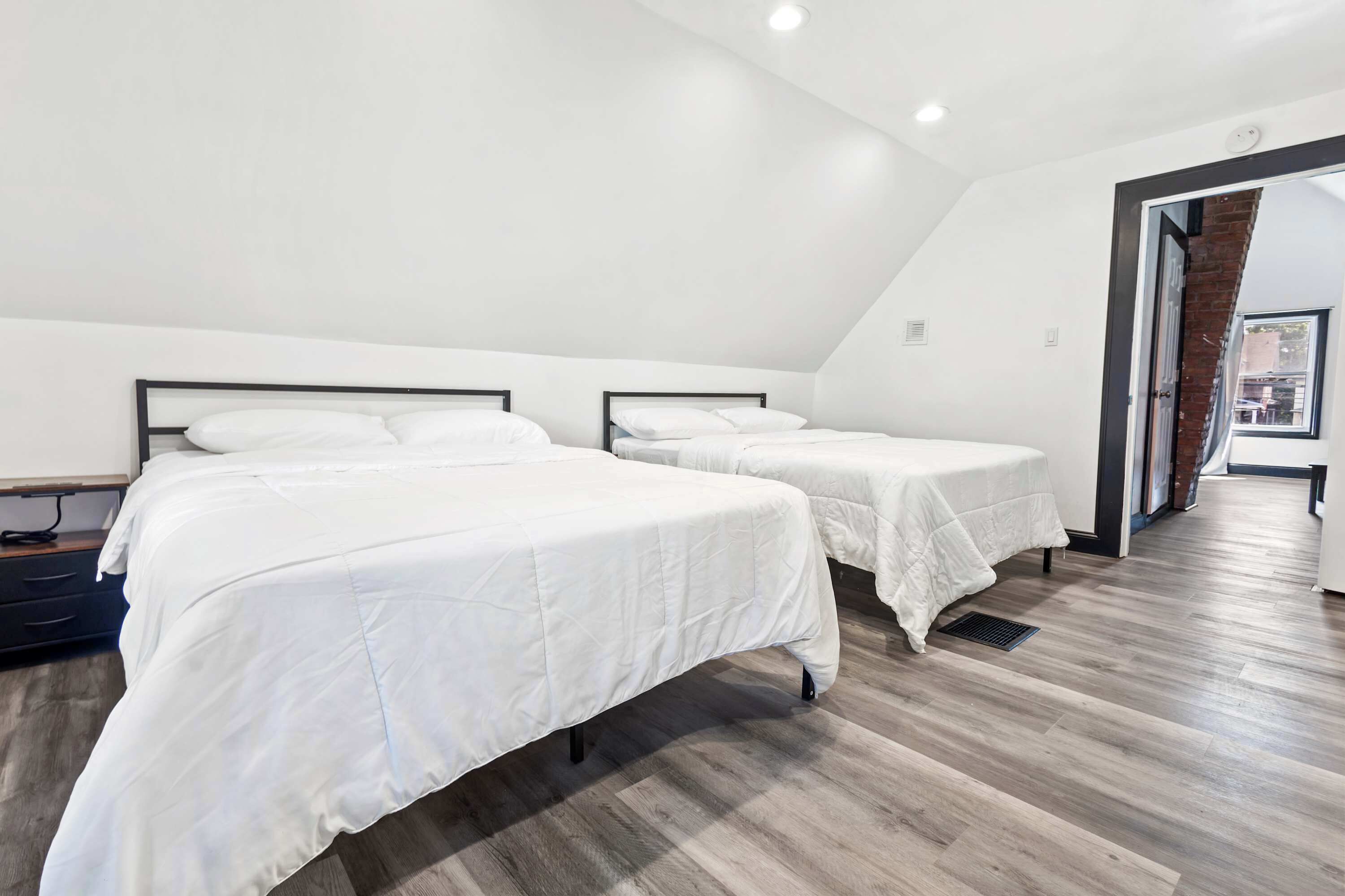 A modern bedroom with two beds, wooden flooring, and a sloped ceiling.
