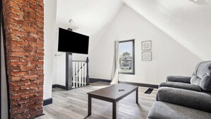 Un salon moderne avec un mur d’accent en briques, un téléviseur à écran plat, un canapé gris et une table basse en bois.